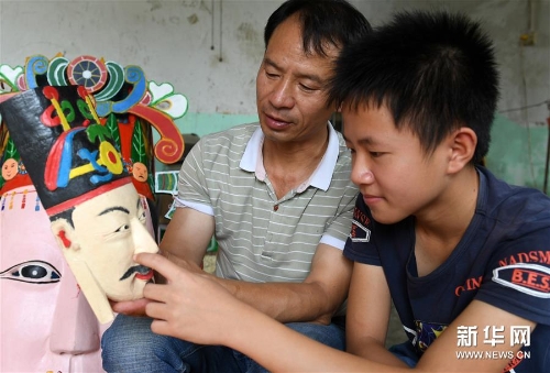 方文展在给儿子方庭源(右)讲述毛南族傩面的雕刻技巧 方文展在给儿子方庭源(右)讲述毛南族傩面的雕刻技巧