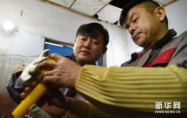 孙云毅（左）在和工人交流一只鸡油黄琉璃艺术品的打磨工艺