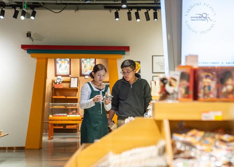 A staff member (L) shows a cultural and creative ornament designed by Yakhore Design Company to a customer at a shop in Lhasa, southwest China's Xizang Autonomous Region, Sept. 29, 2025. (Xinhua/Tenzin Nyida)