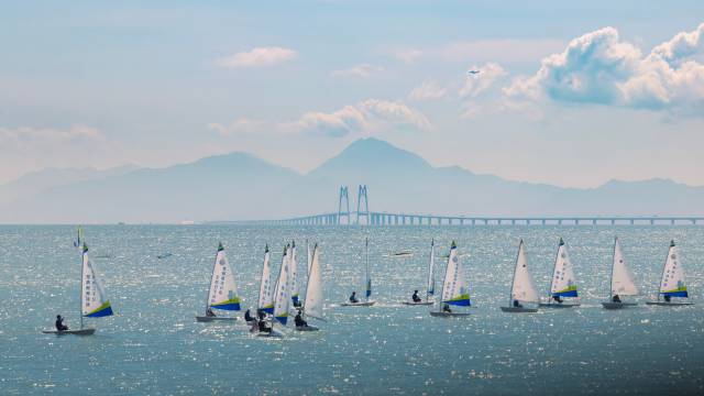 帆影映碧波，远方港珠澳大桥如巨龙卧波，山脉轮廓清晰，景致交融成画。南方+拍客 卓文麟 摄