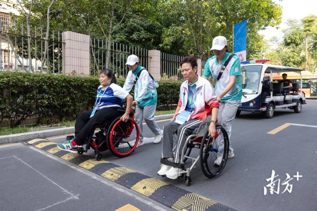 黄丽明(右)与自己的双打搭档吴桂妹在志愿者的协助下前往训练馆练球。 黄丽明(右)与自己的双打搭档吴桂妹在志愿者的协助下前往训练馆练球。