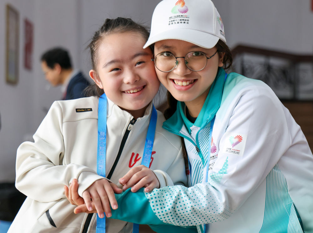 12月13日,山西队选手刘沛颖(左)在等待队友上场时和志愿者合影。新华社记者 刘佳琪 摄